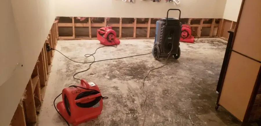 Red air movers and a dehumidifier drying a room with the lower drywall cut away