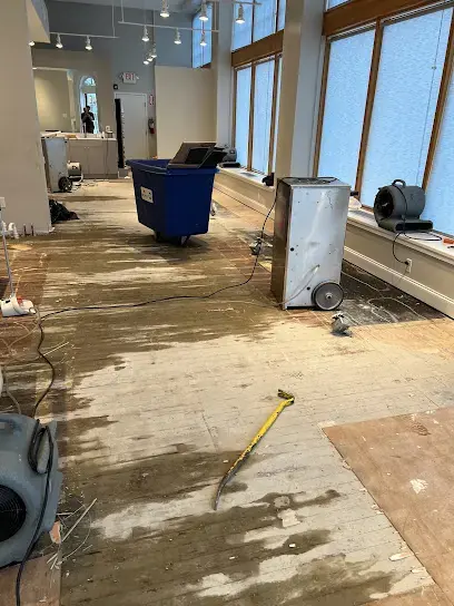 A dehumidifier, an air mover and a bin in a bright room with the flooring pulled up