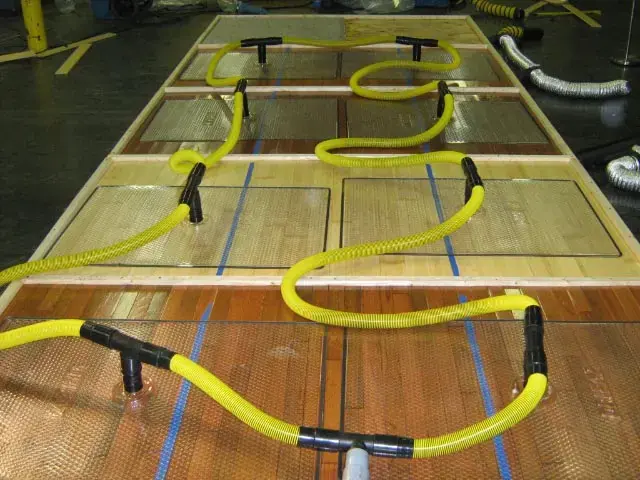 Drying mats and yellow hoses laid across a hardwood floor to pull out trapped moisture