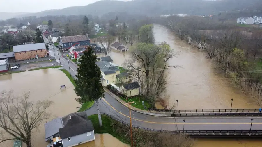 Aerial view of a swollen creek over its banks beside a small town and a road bridge
